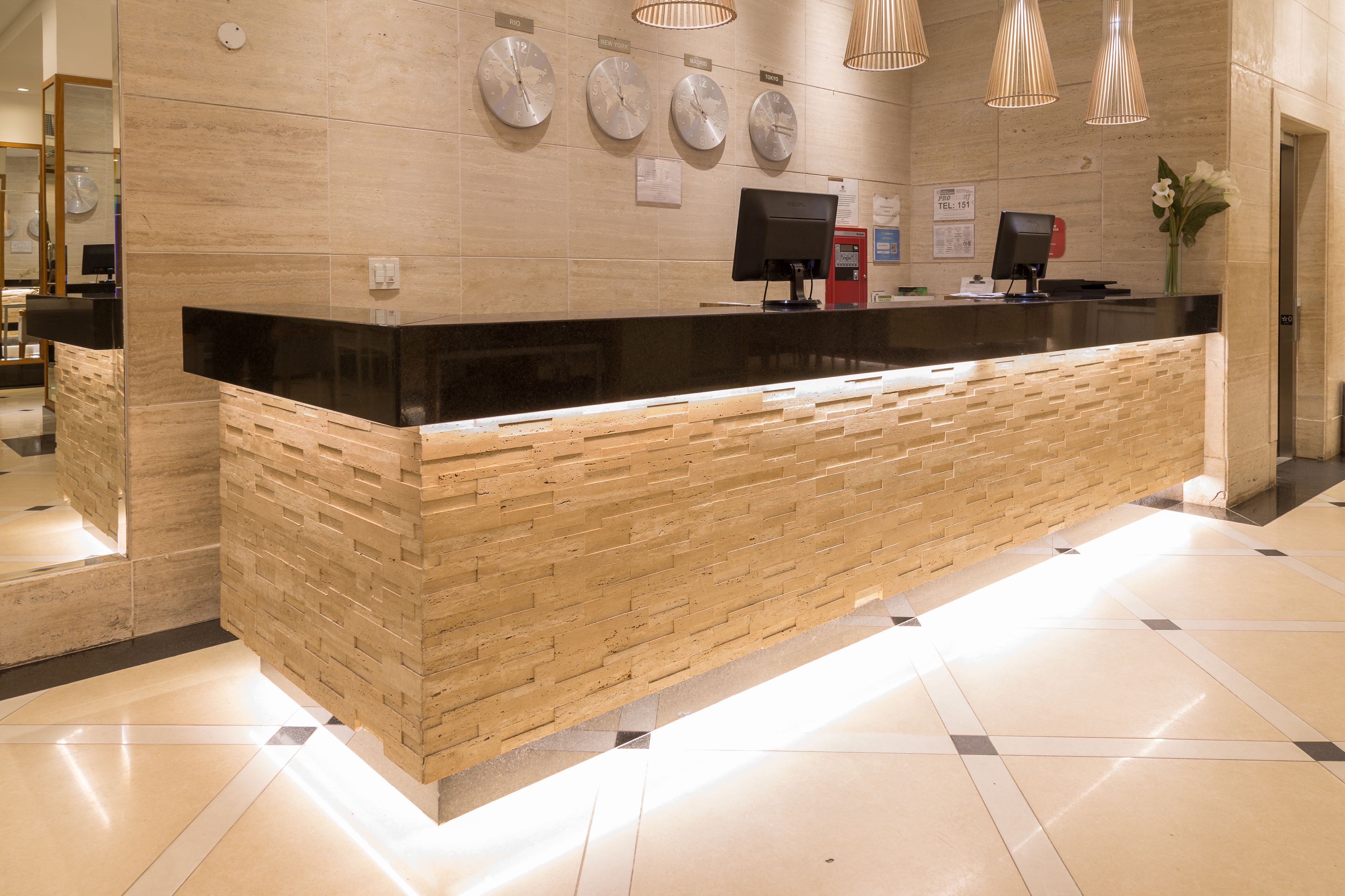 A reception desk with a black top and wooden base, clocks on the wall, and a flower vase.