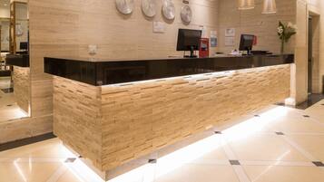 A reception desk with a black top and wooden base, clocks on the wall, and a flower vase.