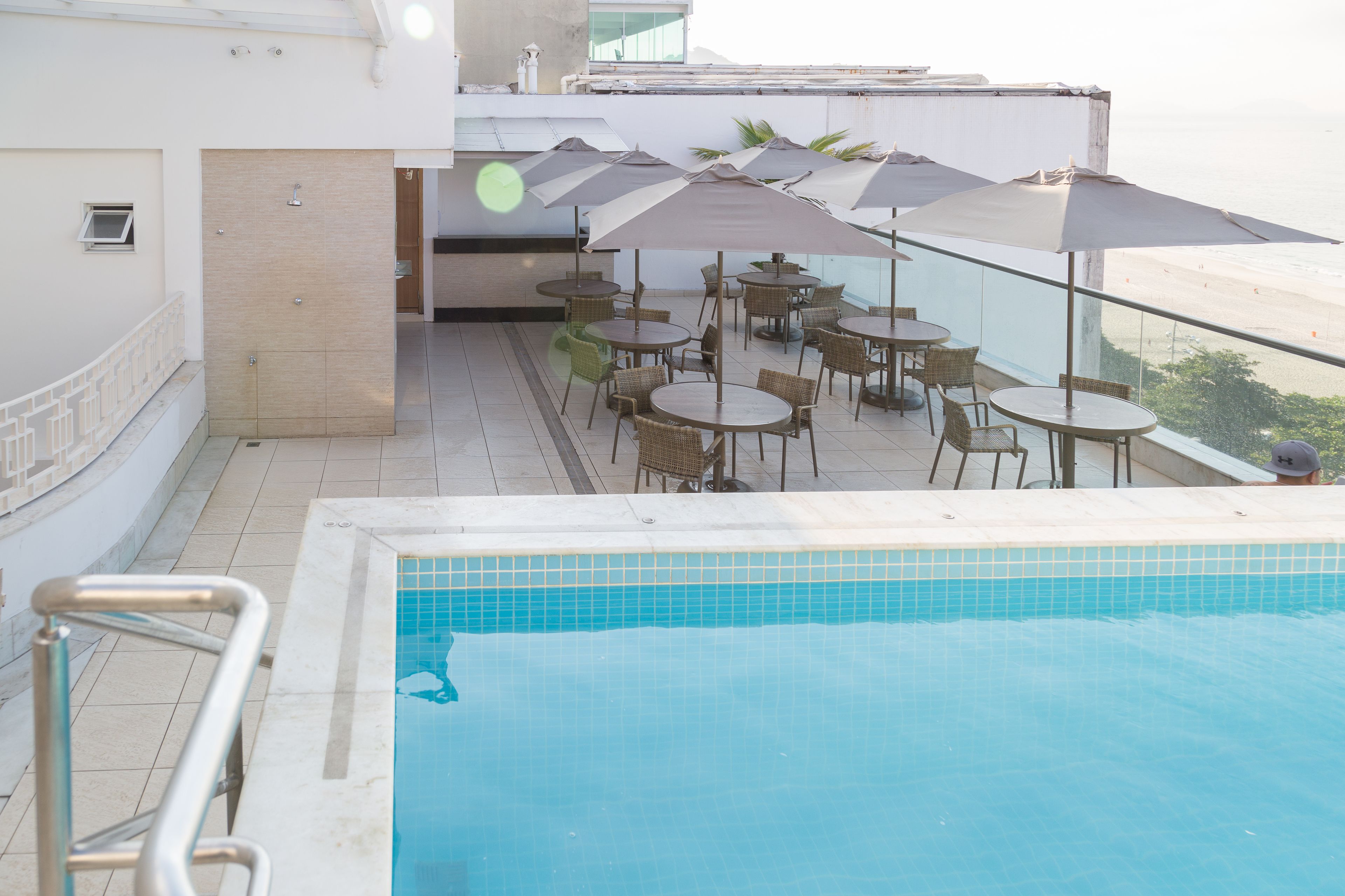 Zona de piscina en la azotea con varias mesas y sillas, una piscina y vistas a la playa.