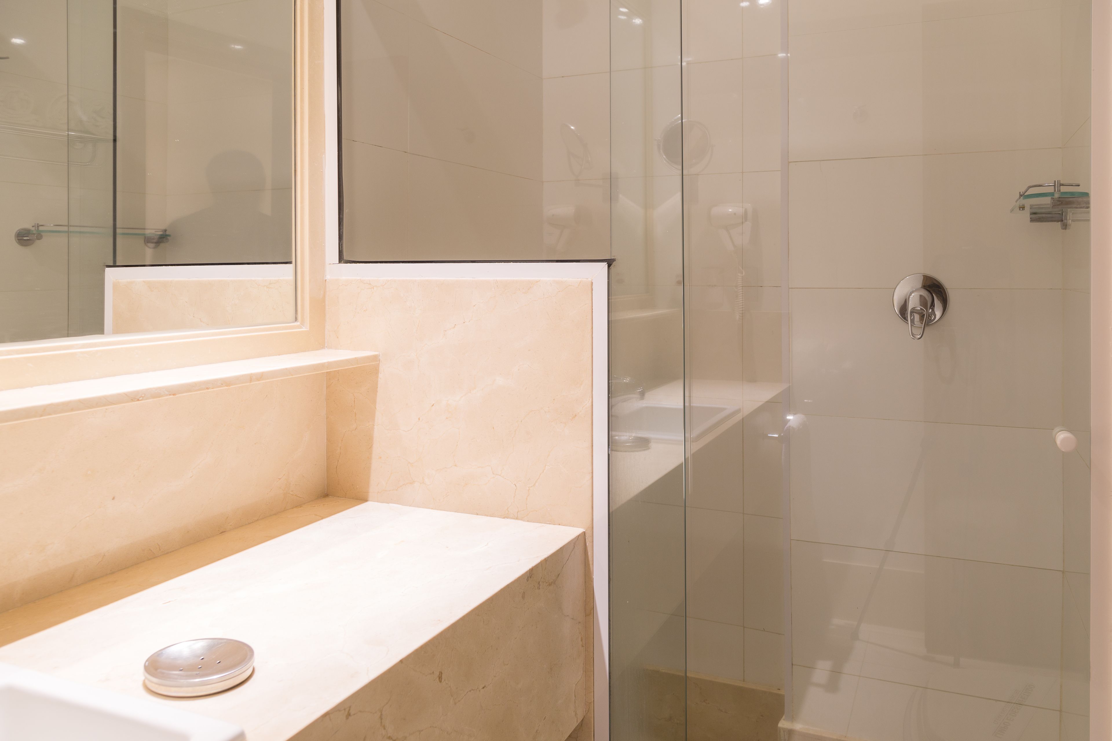 A bathroom with a marble countertop, a glass shower enclosure, and a mirror.