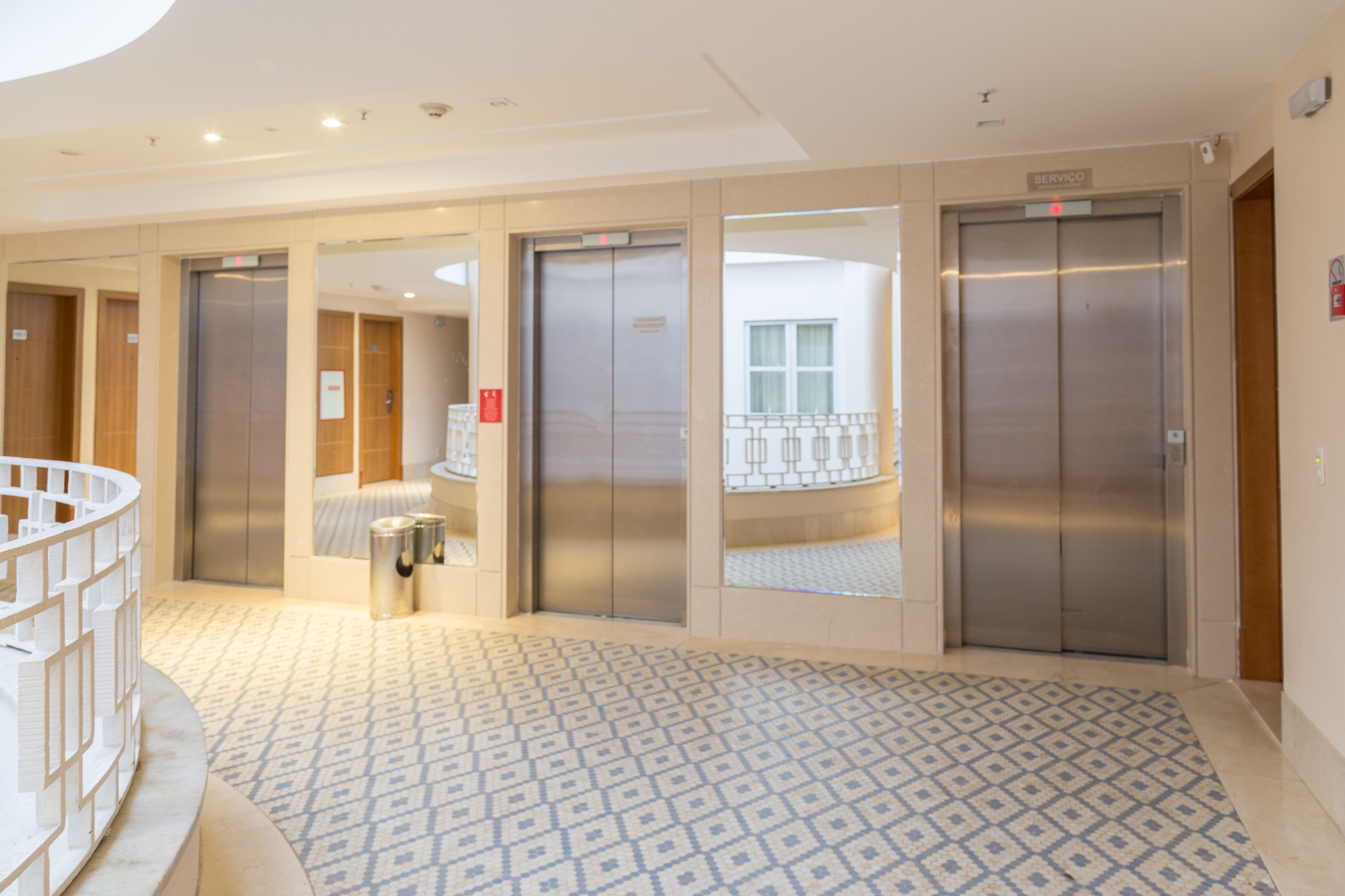 A hotel lobby with a patterned floor, three elevators, and a staircase.