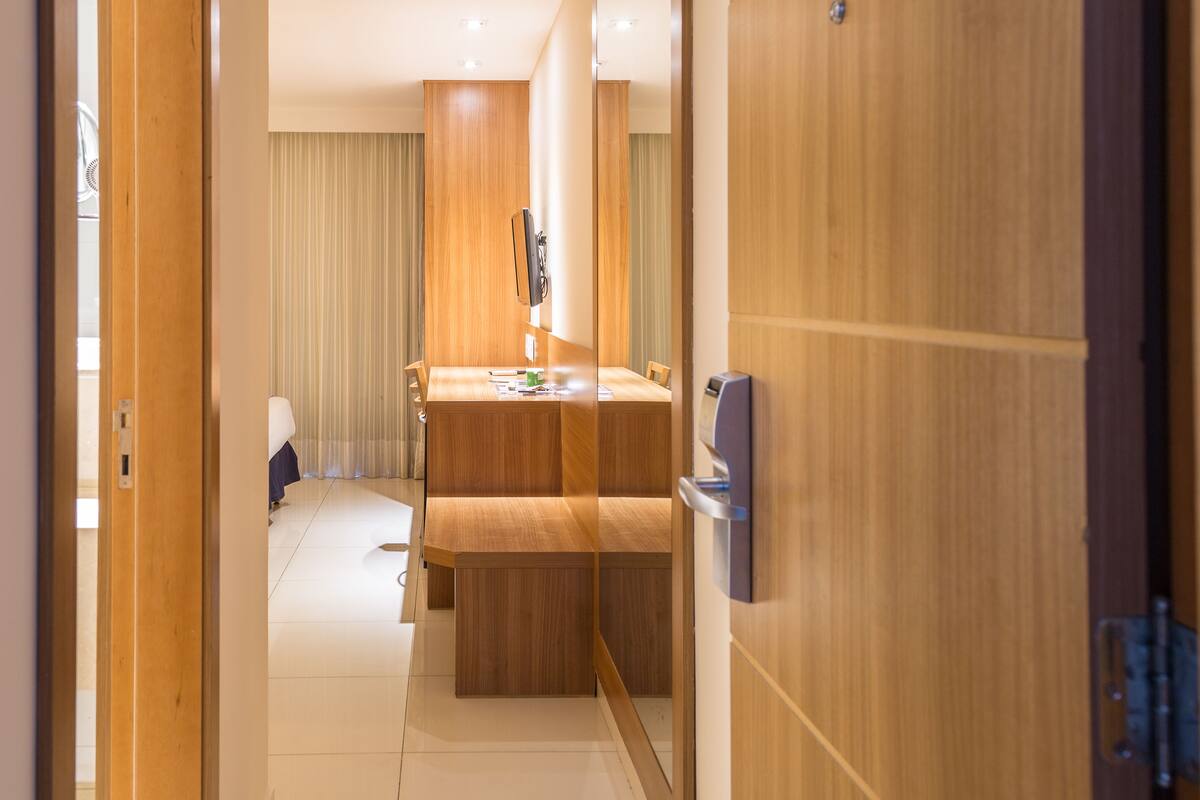 A hotel room with a wooden desk, a flat-screen TV mounted on the wall, and a small seating area with a bench.