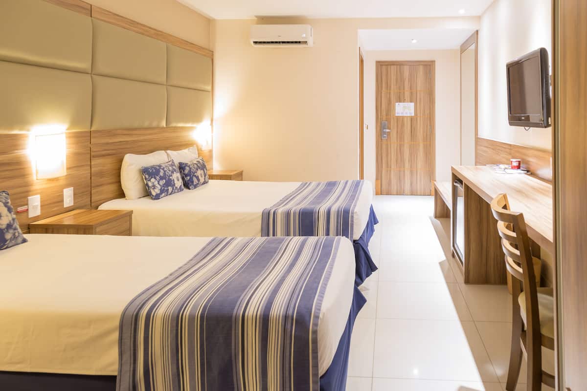 A hotel room with two beds, a desk, a TV, and a mirror.