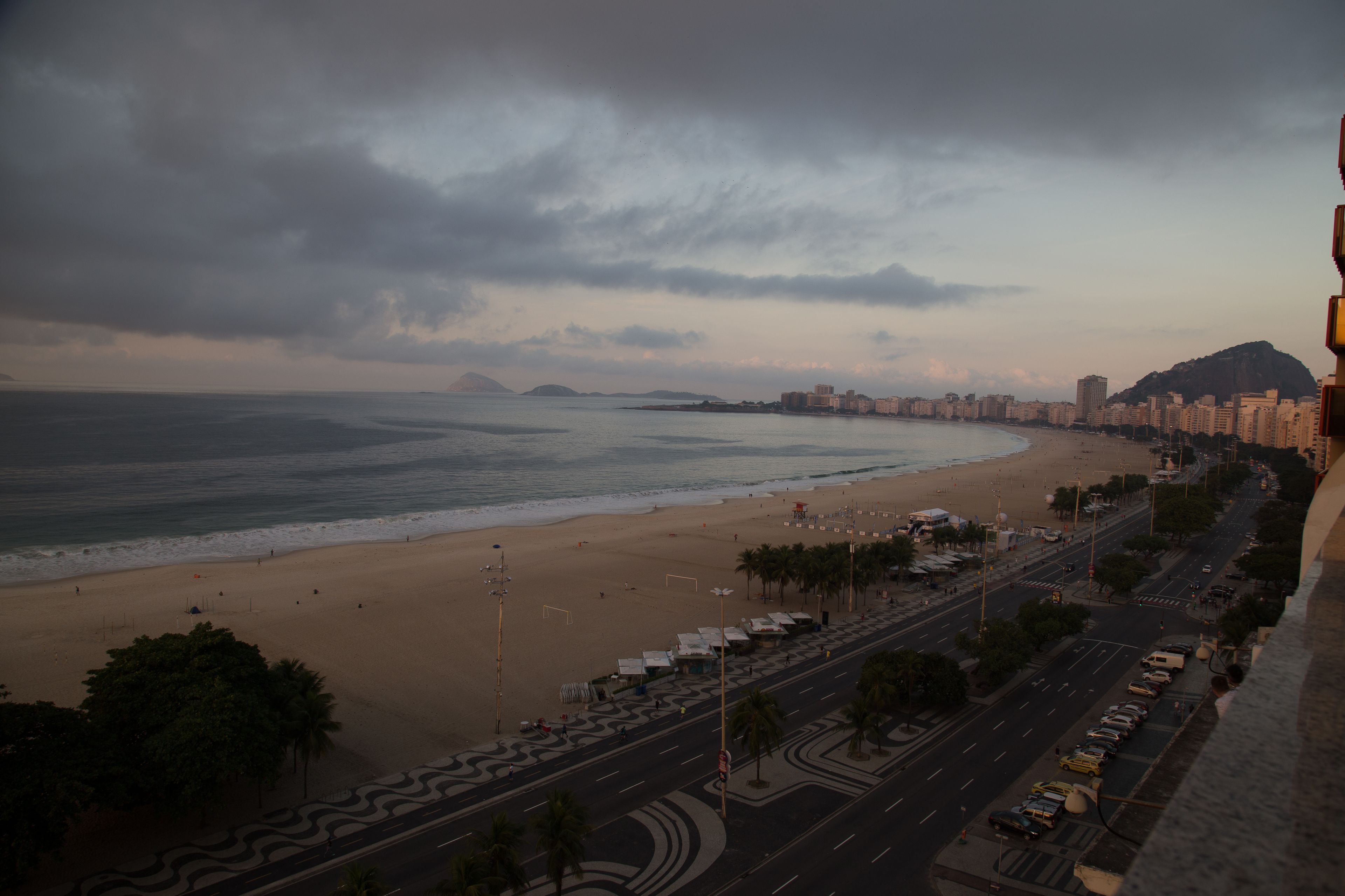 A coastal cityscape with a beach, a road with parked cars, and buildings along the shore.