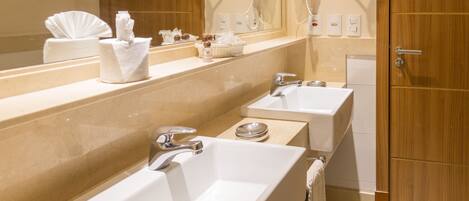 A hotel bathroom with two sinks, a mirror, a hairdryer, and a towel rack.