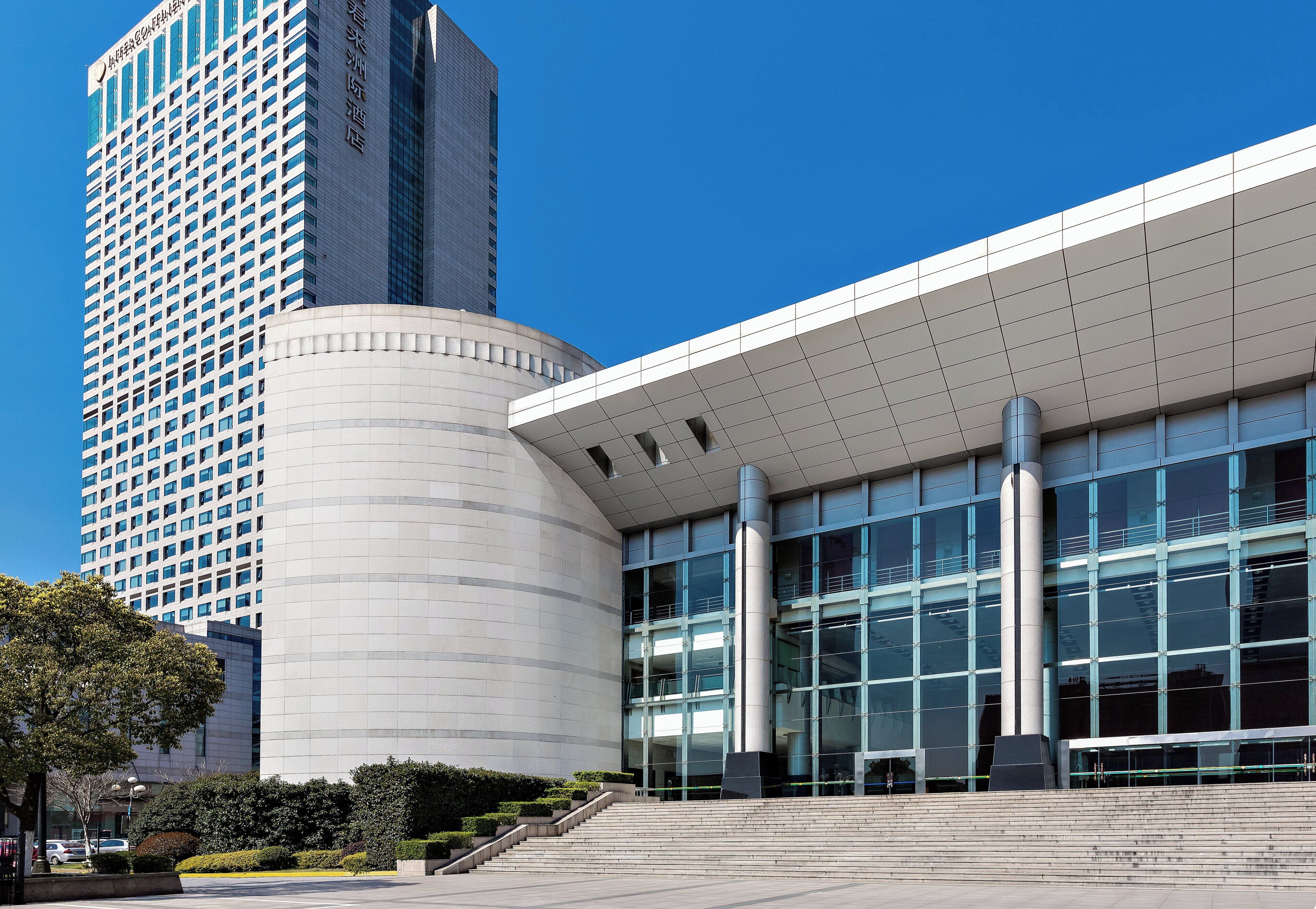 A modern building with a curved facade and large windows, surrounded by a landscaped area with steps leading up to the entrance.