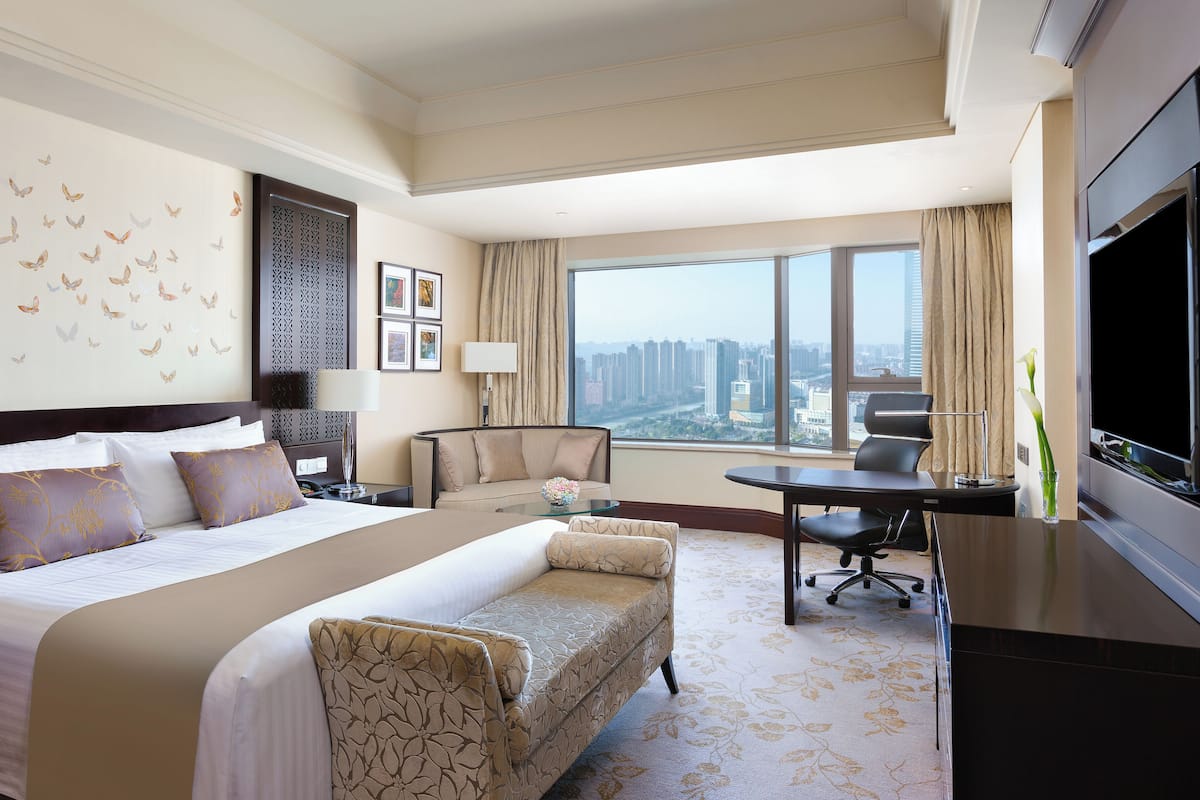 A hotel room with a large bed, a sofa, a desk, and a TV.