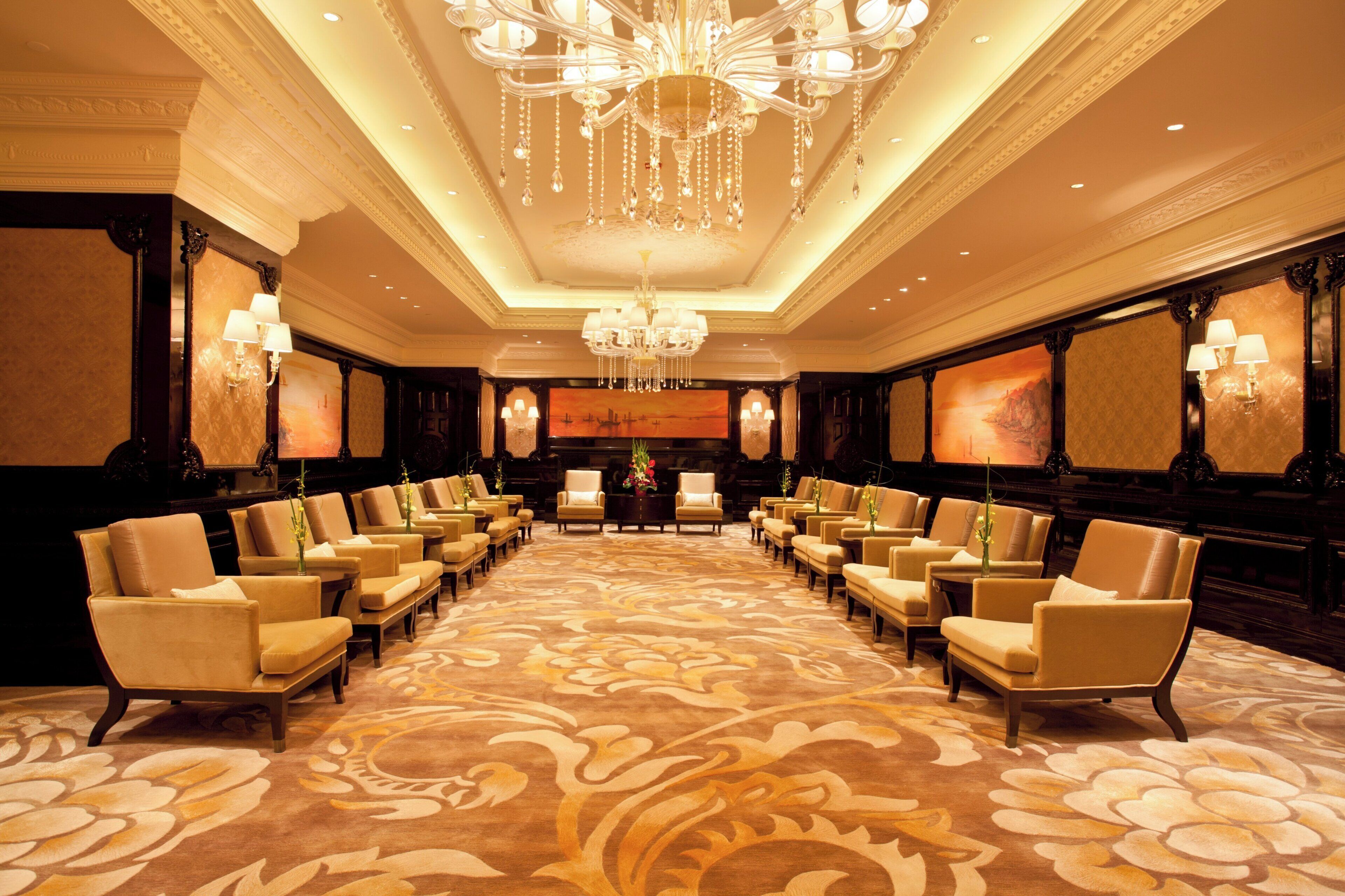 A large conference room with rows of chairs, a chandelier, and wall-mounted lamps.