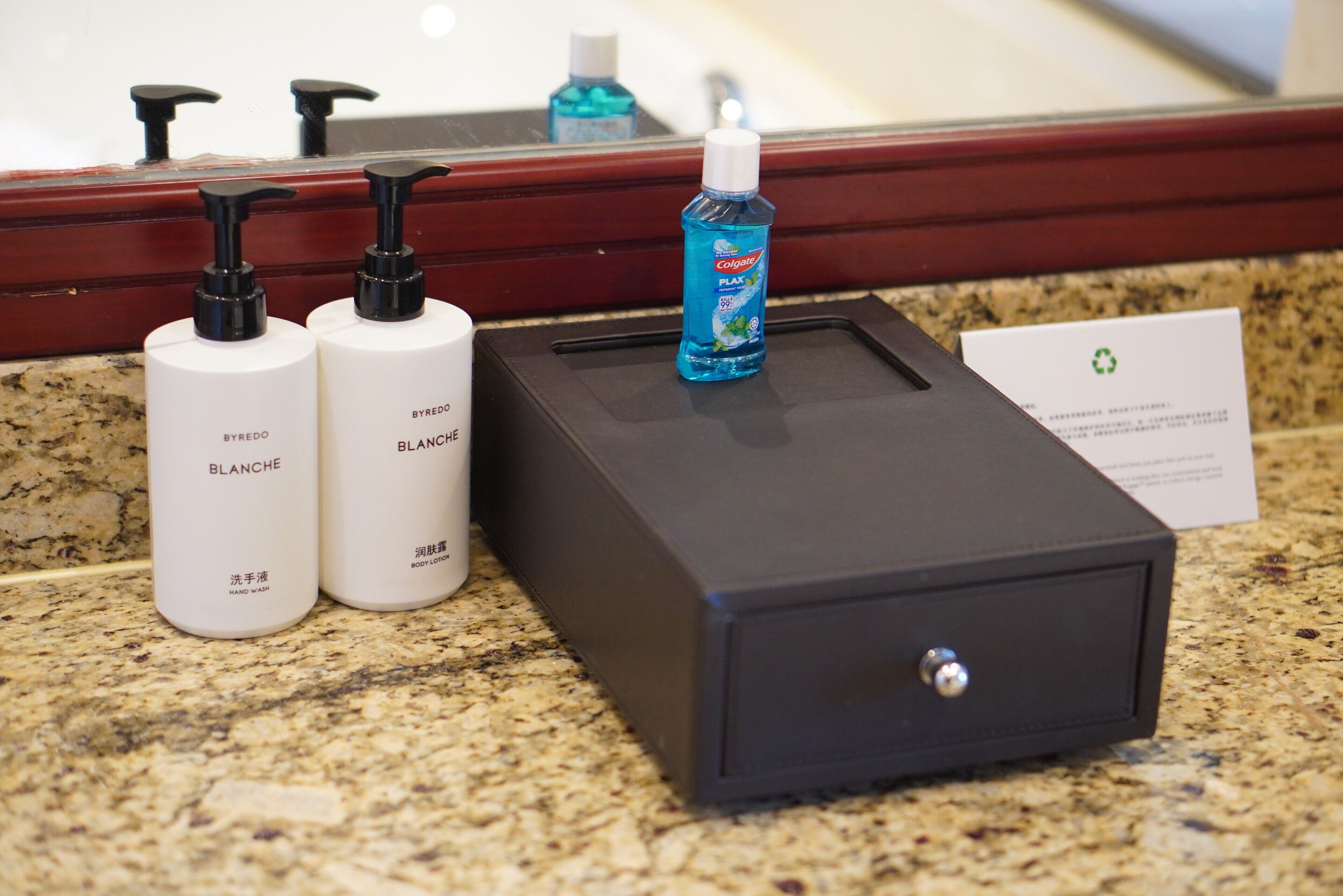 A bathroom counter with hand soap and body lotion bottles, a blue toothbrush, and a black storage box.
