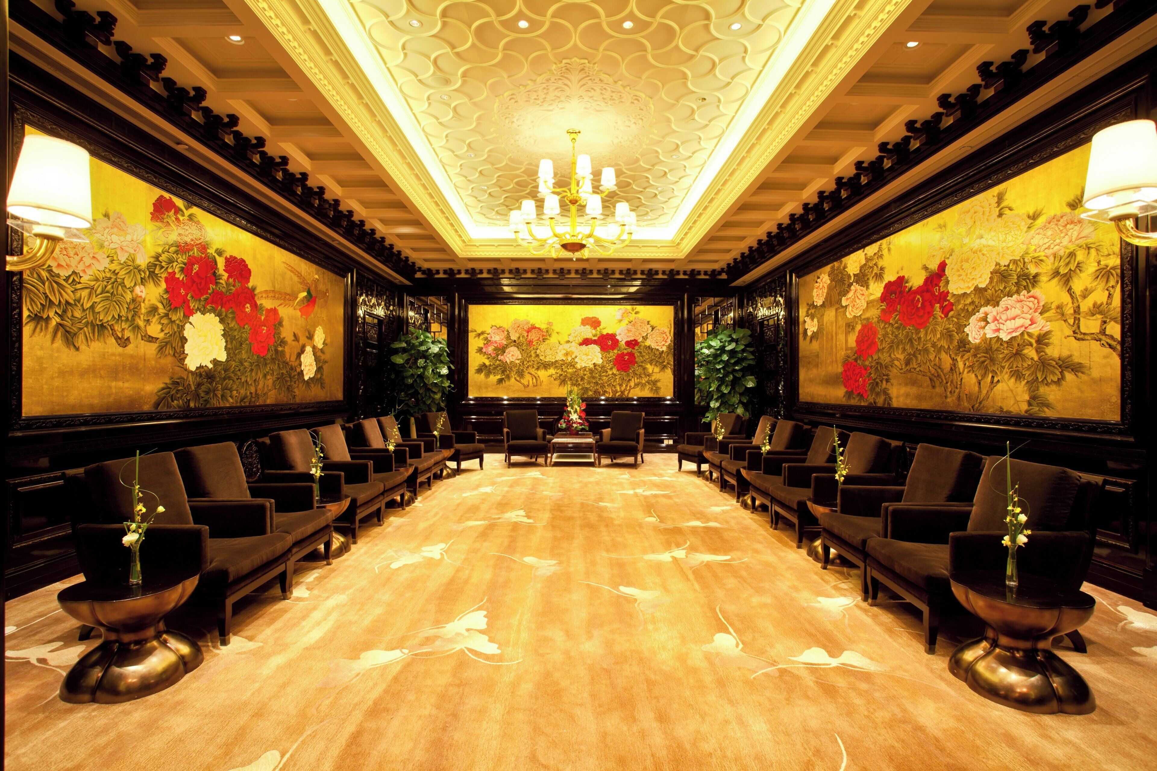 Una sala elegante con una mesa larga, múltiples sillas y pinturas florales en las paredes.