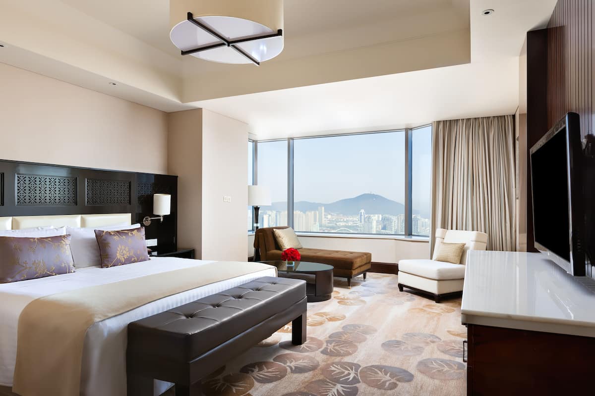 A spacious hotel room with a large bed, a sofa, a coffee table, and a TV.