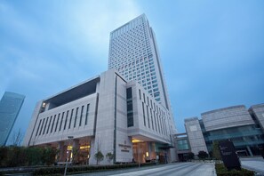A modern building with a prominent entrance and a tall skyscraper in the background. - Intercontinental Wuxi by IHG (Wuxi)
