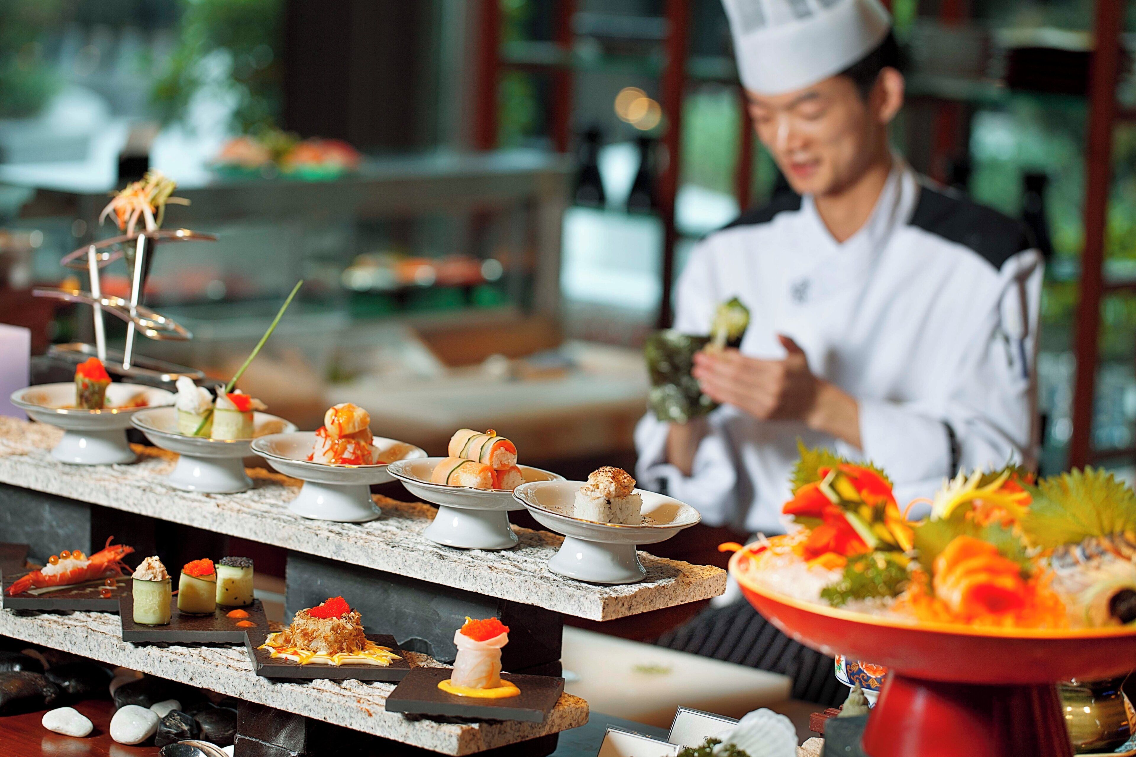 A chef preparing food in a kitchen with various dishes displayed on a counter.