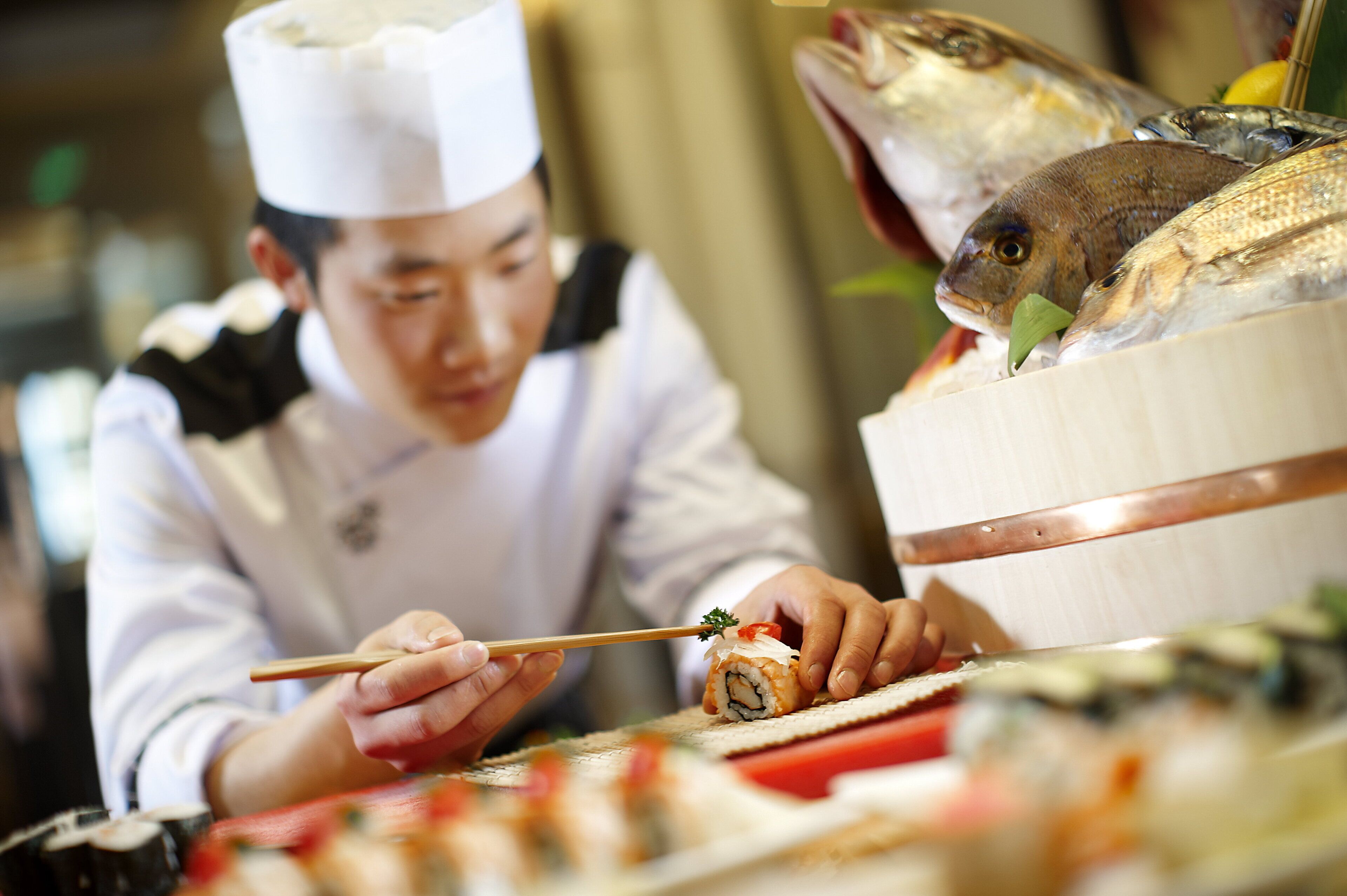 A chef preparing sushi with a fish on the counter.