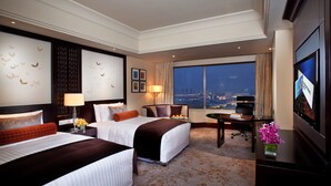 Una habitación de hotel con dos camas, un escritorio, un televisor y un ventanal con vistas a la ciudad.