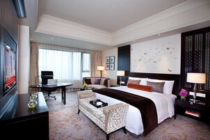 Una habitación de hotel con una cama grande, un escritorio con una computadora portátil, un sofá y un televisor.