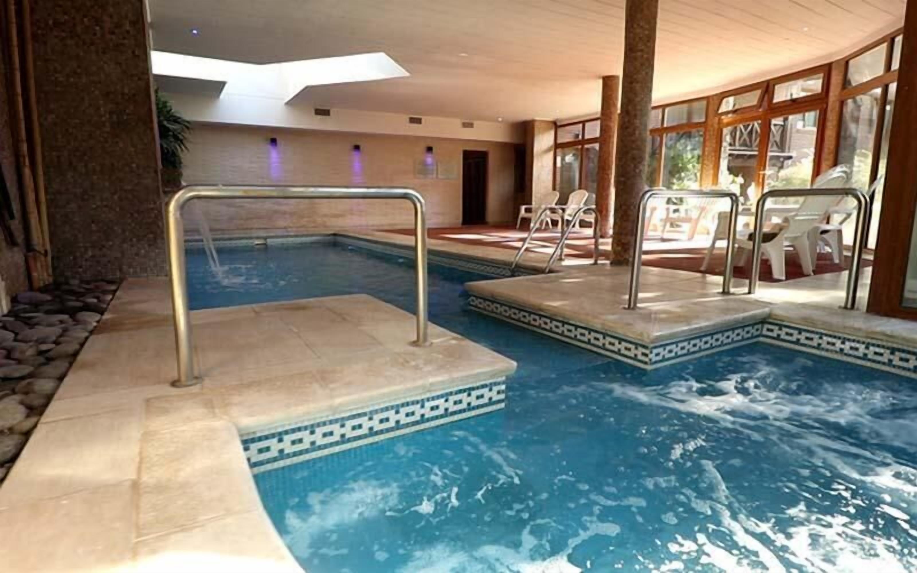 Una piscina interior con borde de azulejos, un trampolín y sillones de descanso.