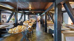 A spacious restaurant with high ceilings and exposed beams, featuring long communal tables and a hanging bread basket. - Relais & Châteaux Landhaus Stricker (Sylt)