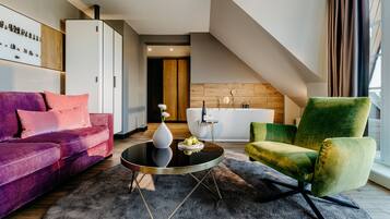 A modern living room with a purple sofa, a green armchair, a round coffee table, and a kitchen area in the background.