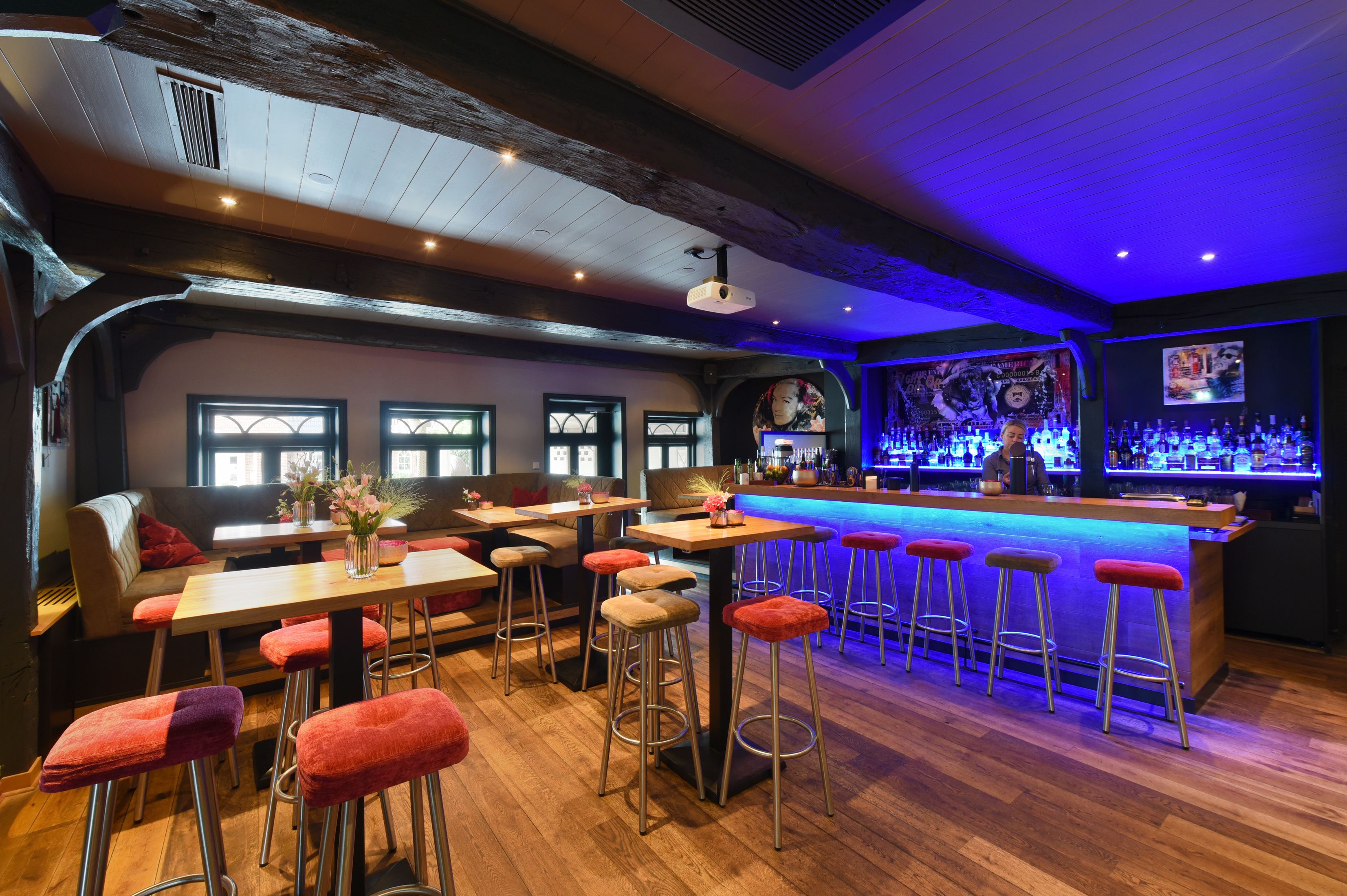 Un espace bar doté d’un plancher en bois, de tabourets de bar rouges et d’un comptoir.