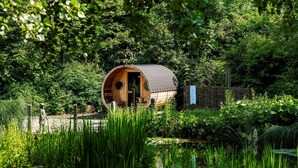 A wooden cabin with a curved roof nestled in a lush garden. - Relais & Châteaux Landhaus Stricker (Sylt)