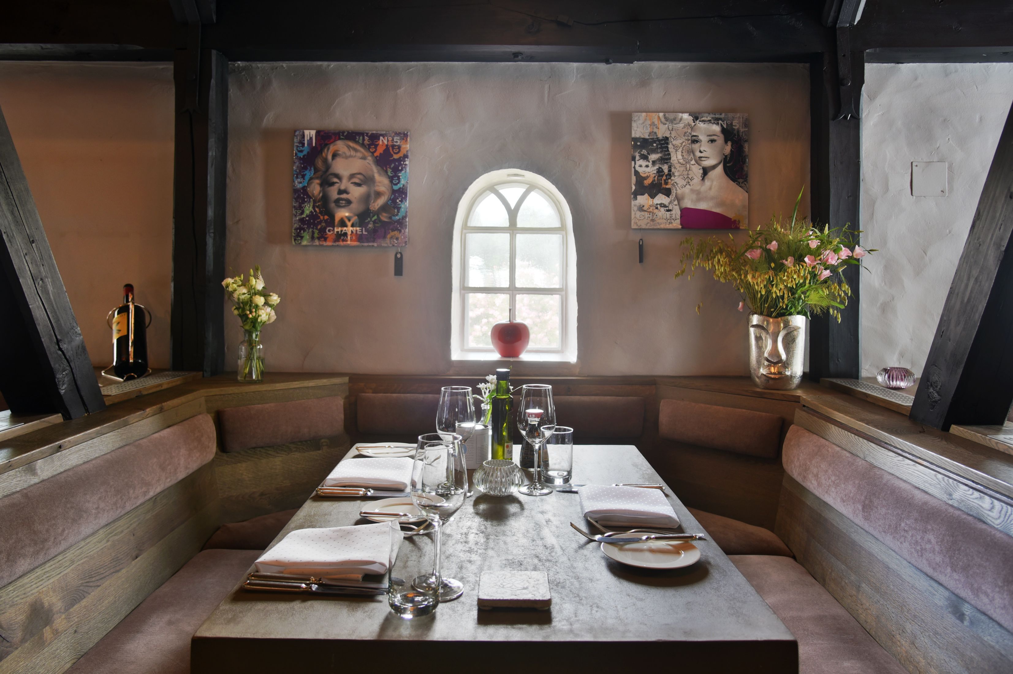 Un comedor con una mesa preparada para cuatro personas, bancos, un ventanal con vistas y obras de arte en las paredes.