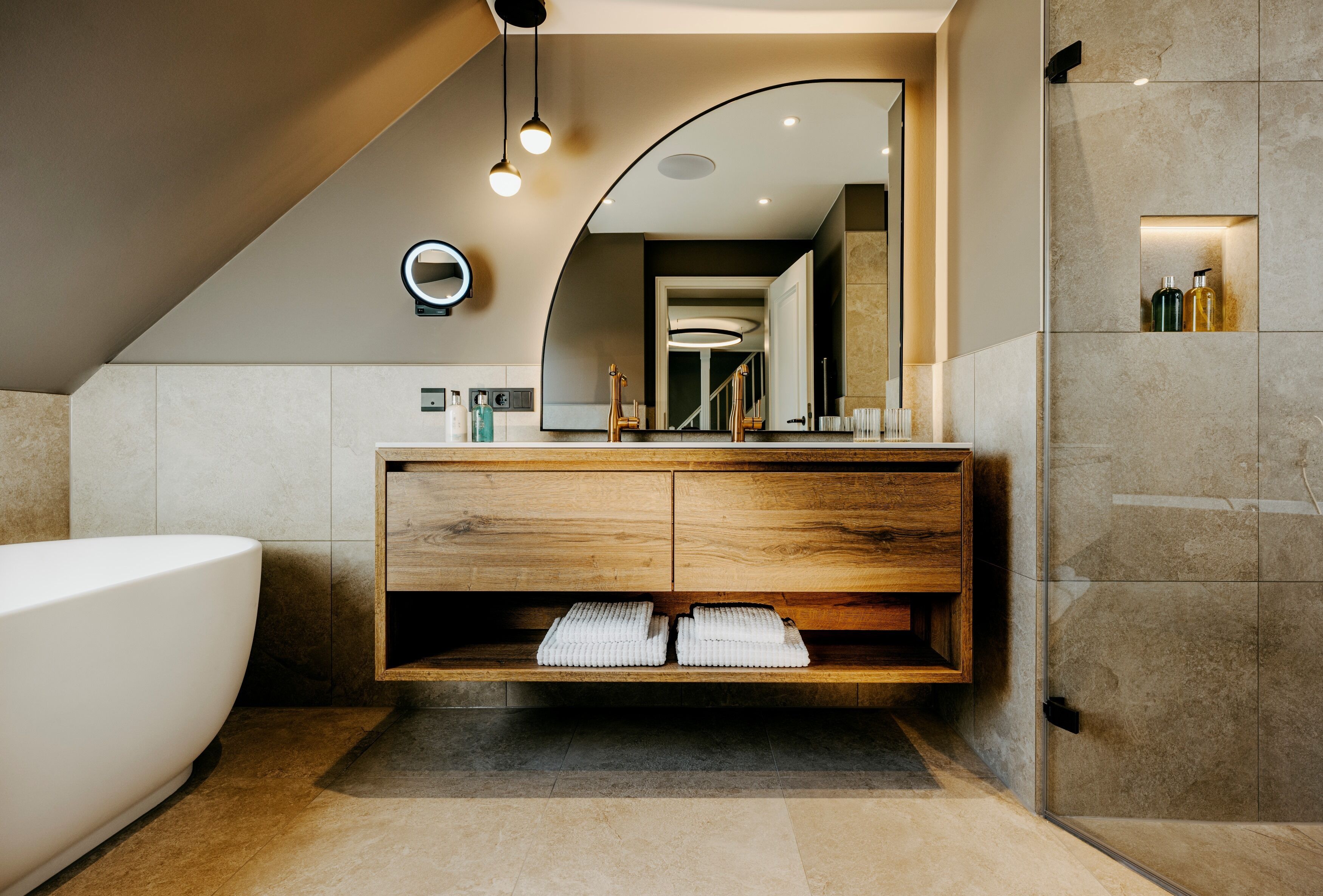 A modern bathroom with a freestanding bathtub, wooden vanity, and a large mirror.