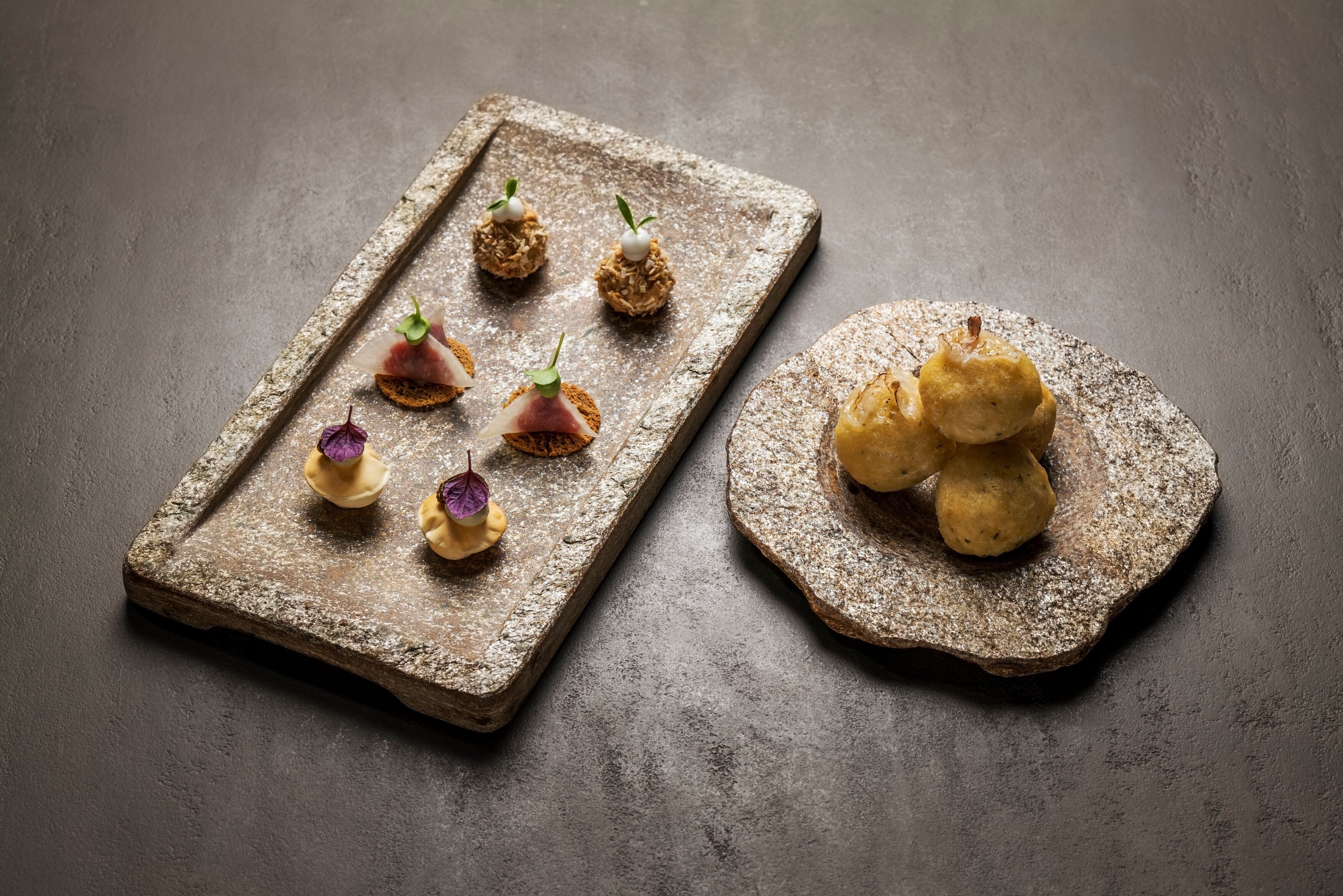 Une planche de service rustique en bois, sur laquelle sont disposés divers amuse-gueule, dont certains à base de légumes verts et d’autres à base de viande, le tout présenté sur une surface texturée.