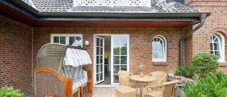 Une maison en briques avec un balcon, un espace extérieur aménagé et couvert avec des meubles en osier, et un petit jardin.