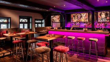 Un espace bar avec des tables en bois et des tabourets rouges rembourrés, un comptoir de bar avec des bouteilles et des œuvres d’art accrochées aux murs.