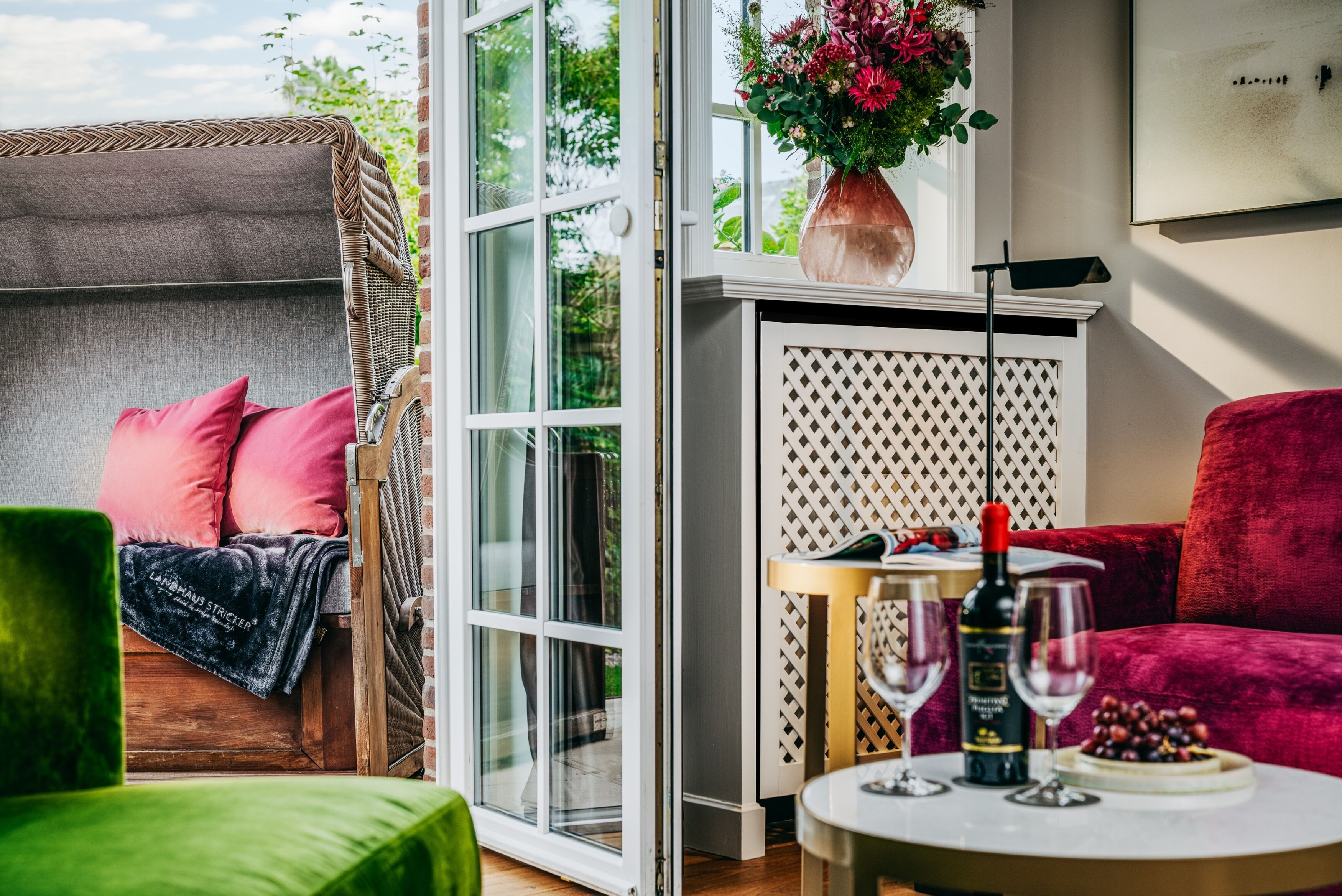 Et hyggeligt værelse med en grøn lænestol, en rød sofa og et bord med vinglas og en flaske vin.