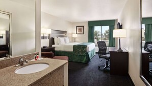 A hotel room with a bed, a desk, a chair, a sink, and a large mirror. - Travelodge by Wyndham McAlester (McAlester)
