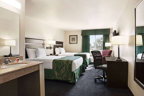 Une chambre d’hôtel avec deux lits, un bureau, une chaise, une lampe de bureau, un miroir et un lavabo.