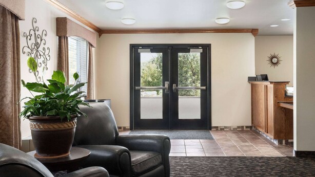 A hotel lobby with a reception desk, a potted plant, leather seating, and a large glass door leading outside. - Travelodge by Wyndham McAlester (McAlester)