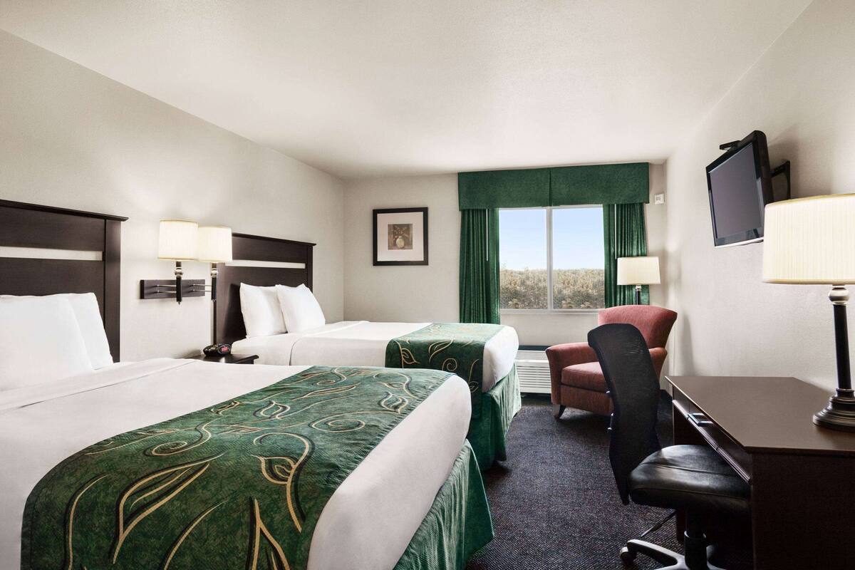 A hotel room with two beds, a desk, a chair, a TV, and a window with curtains.