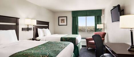 A hotel room with two beds, a desk, a chair, a TV, and a window with curtains.