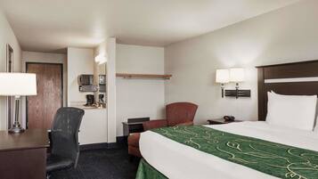 A hotel room with a bed, desk, chair, and a small kitchenette area.