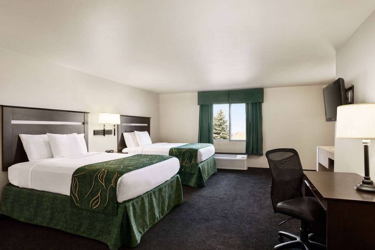 A hotel room with two beds, a desk, a chair, a TV, and a window with curtains.