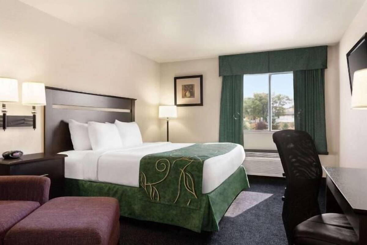 A hotel room with a bed, two bedside lamps, a desk, a chair, and a window with curtains.