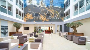 A spacious lobby with modern seating, a large mural, and a view of the water. - Hotel Drazica (Krk)