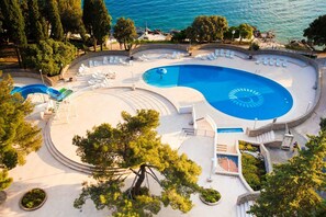 Una amplia piscina con diseño circular, rodeada de sillas de descanso y una zona ajardinada con árboles.