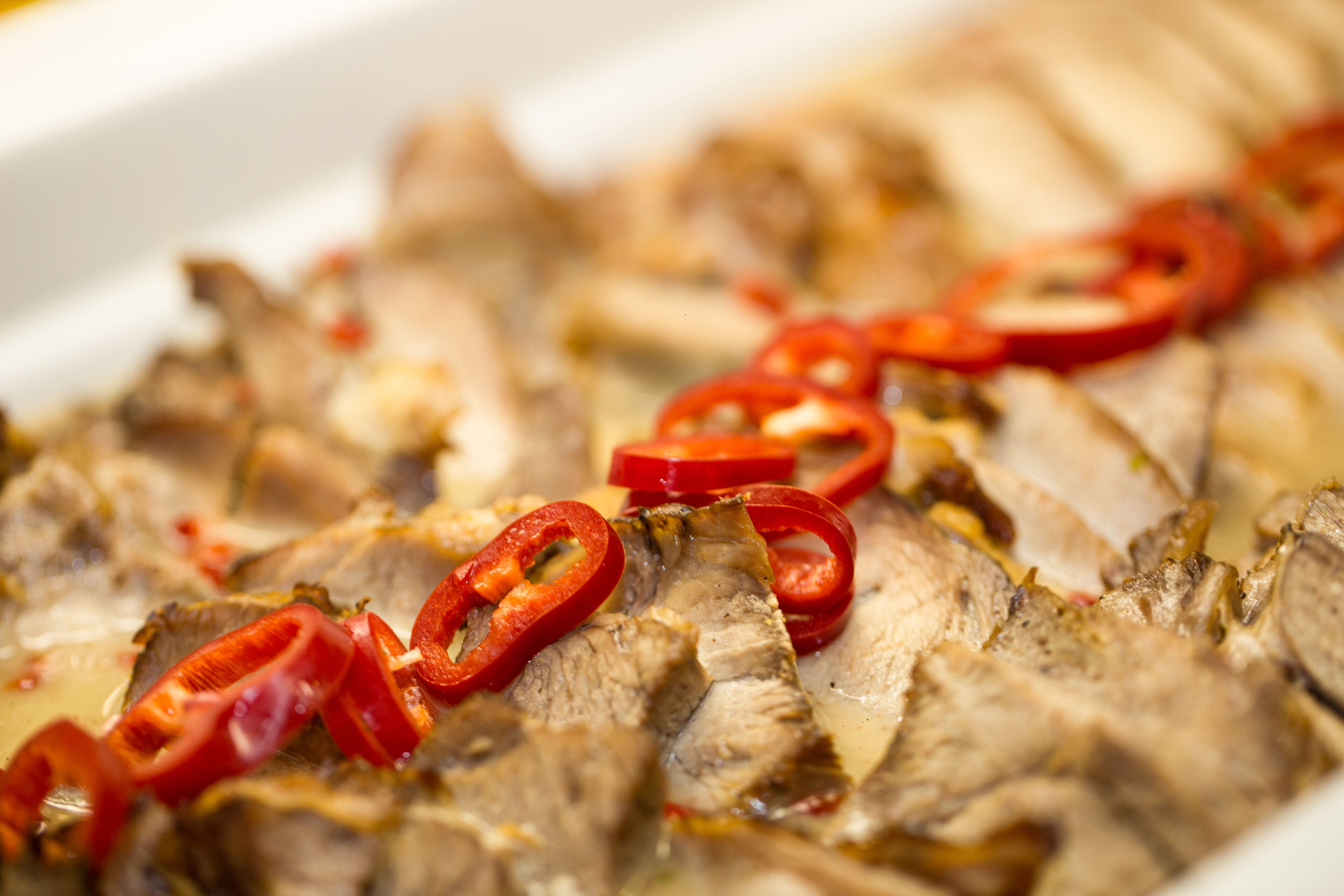 Un plat composé de viande coupée en tranches et de piments rouges.