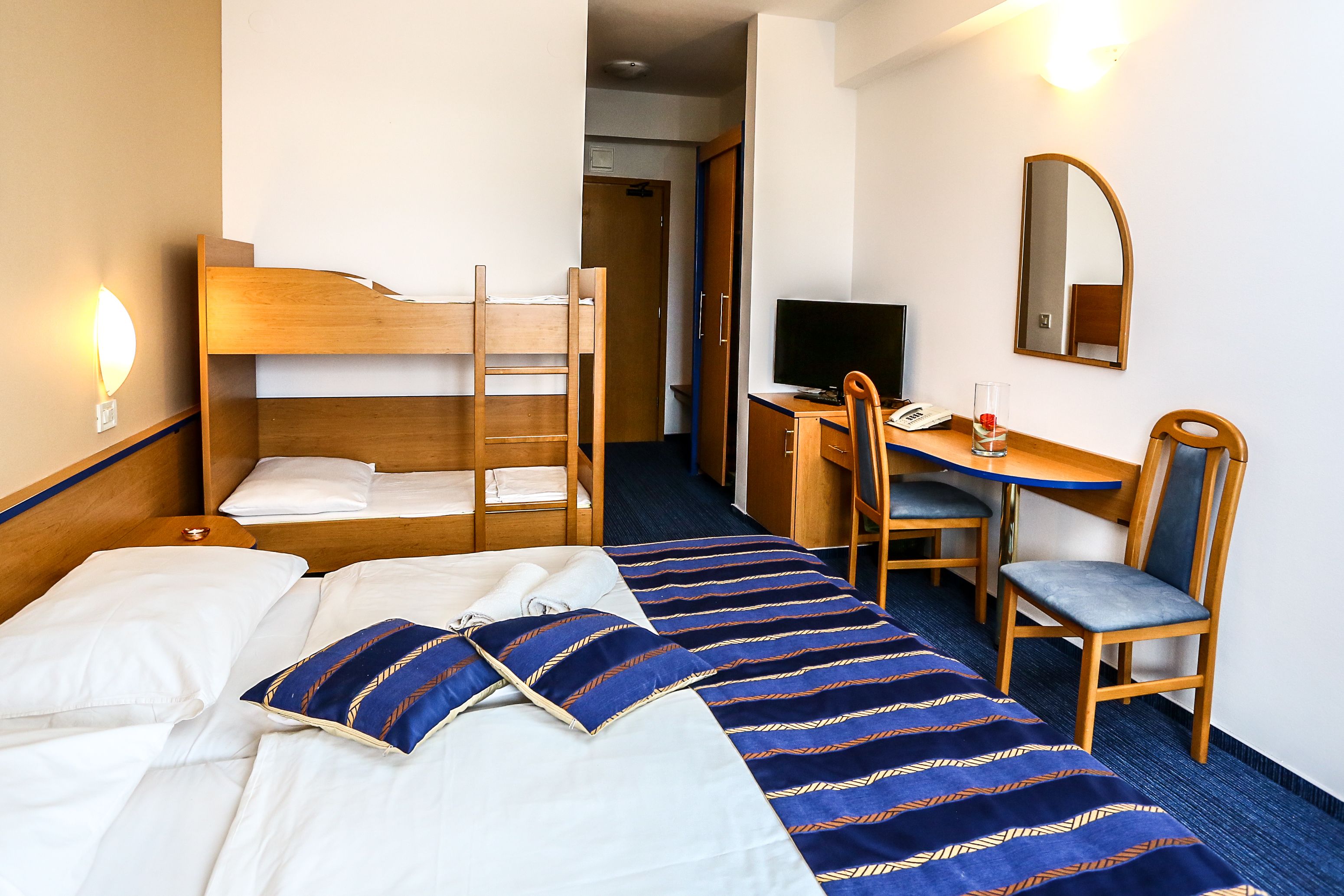 Une chambre d’hôtel avec un lit superposé, un bureau avec une chaise, une télévision et un miroir.