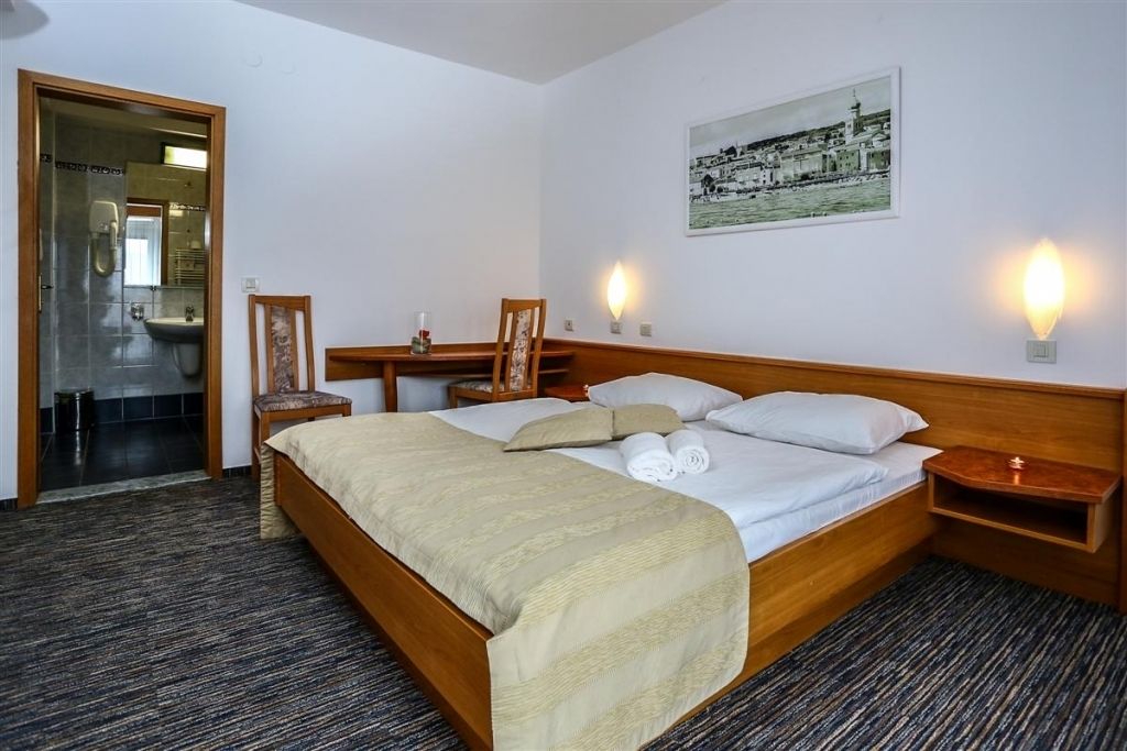 A hotel room with a large bed, a wooden headboard, a nightstand, a framed picture, and a wall-mounted light.