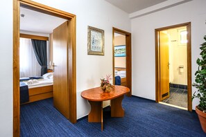 A hotel room with a bed, a wooden table with a vase, a framed picture on the wall, and a potted plant.