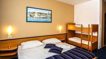 Habitación de hotel con una cama individual, dos mesitas de noche, una cama litera de madera y un cuadro colgado en la pared de un pueblo costero.