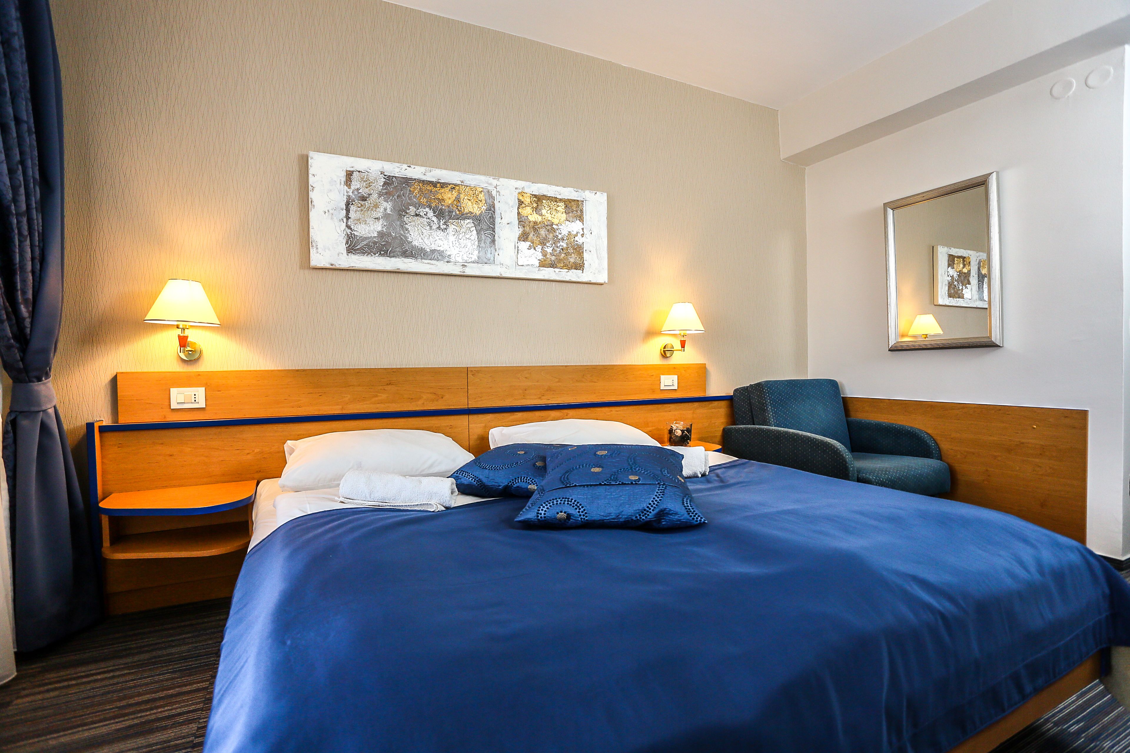 Ein Hotelzimmer mit einem großen Bett, zwei Nachttischlampen, einem Sessel und einem Bild an der Wand.