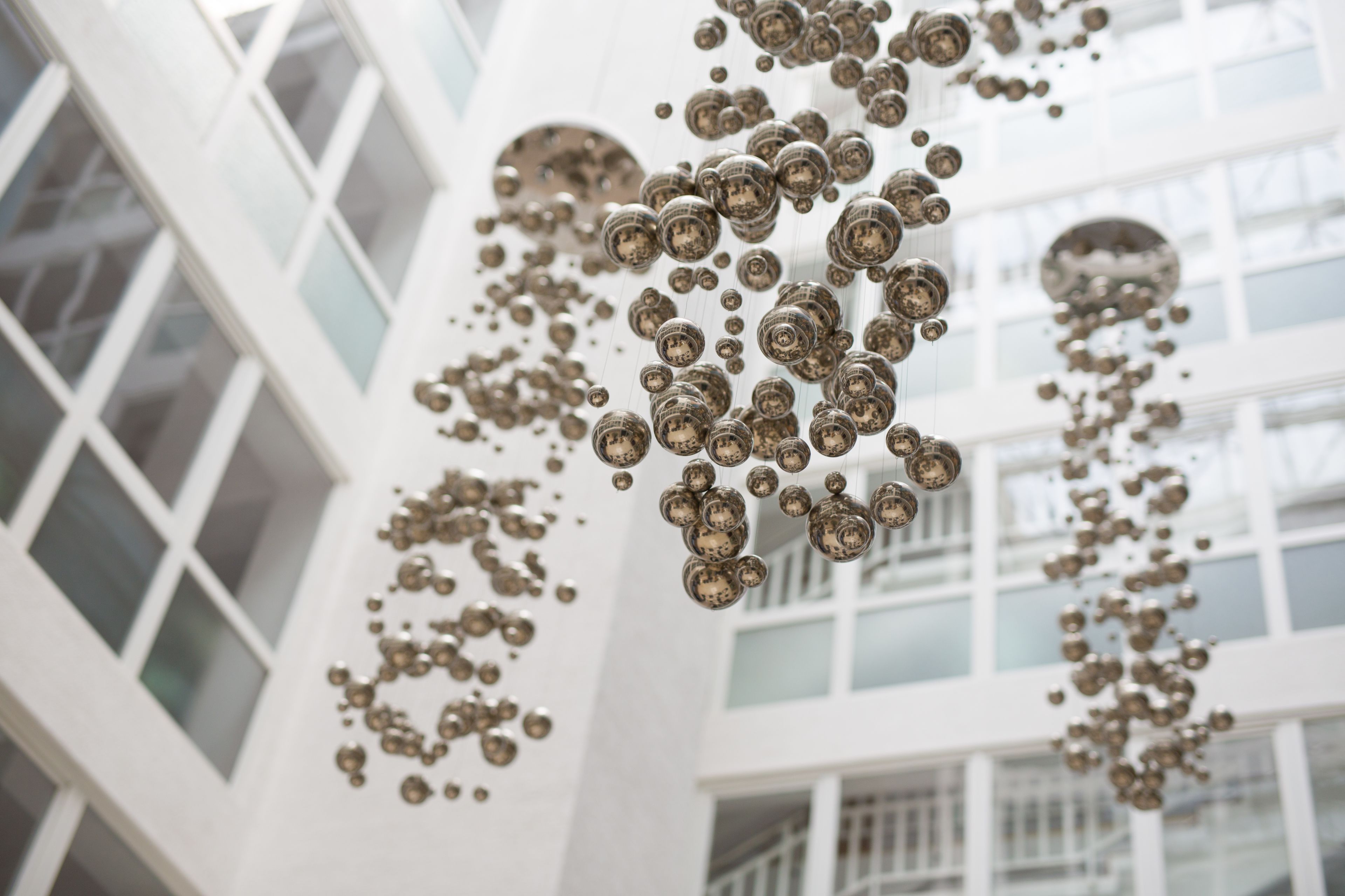 Interior de un edificio moderno con ventanas amplias y decoraciones metálicas esféricas colgando del techo.