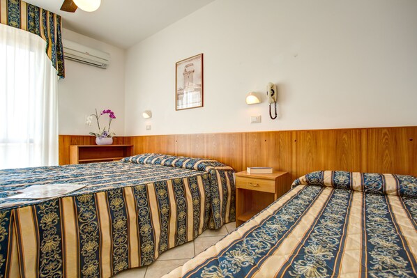 Habitación de hotel con dos camas, cabecero de madera, mesita de noche con lámpara, cuadro en la pared y equipo de aire acondicionado.