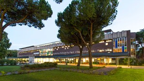 A modern building with a flat roof, large windows, and a central courtyard with benches and trees. - Hotel Genzianella (Cervia)